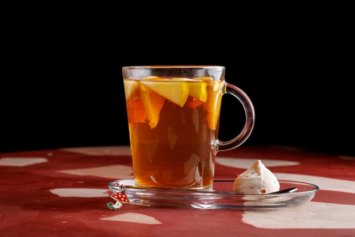 Гарячий чай зі скибками апельсина у скляному кухлі